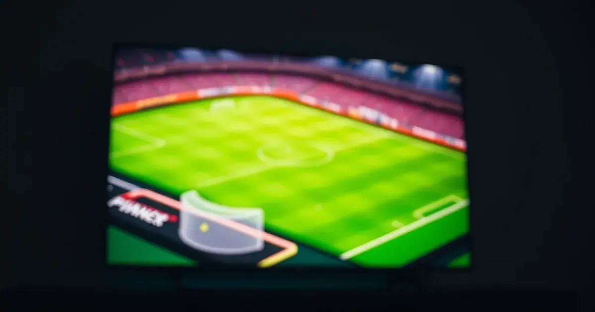 Apple TV 4K box and remote on a console beneath a television showing a glowing football pitch in a dark, premium living room